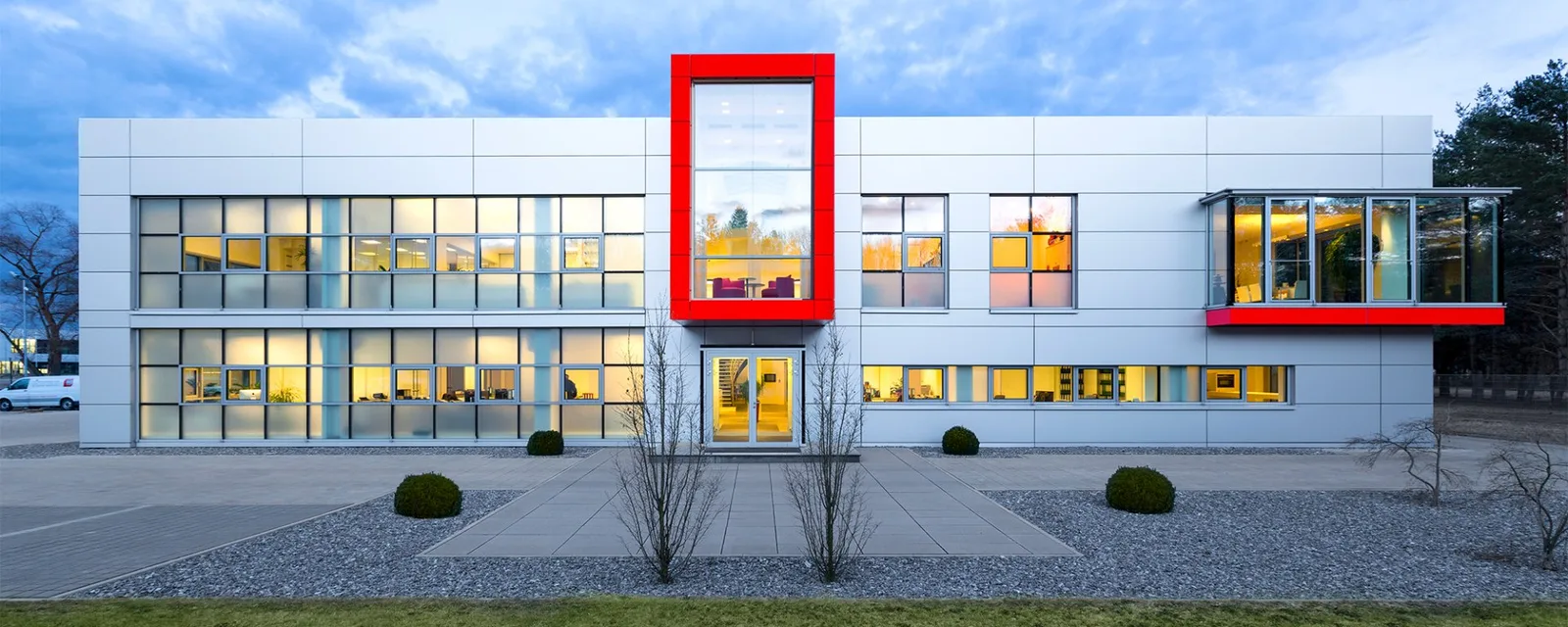 Niederlassung Ingolstadt im Abendlicht, helle Fassade mit großem rotem Rahmen um den Eingang